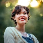 Portrait of a cheerful young woman smiling outdoors with soft, vibrant lighting.